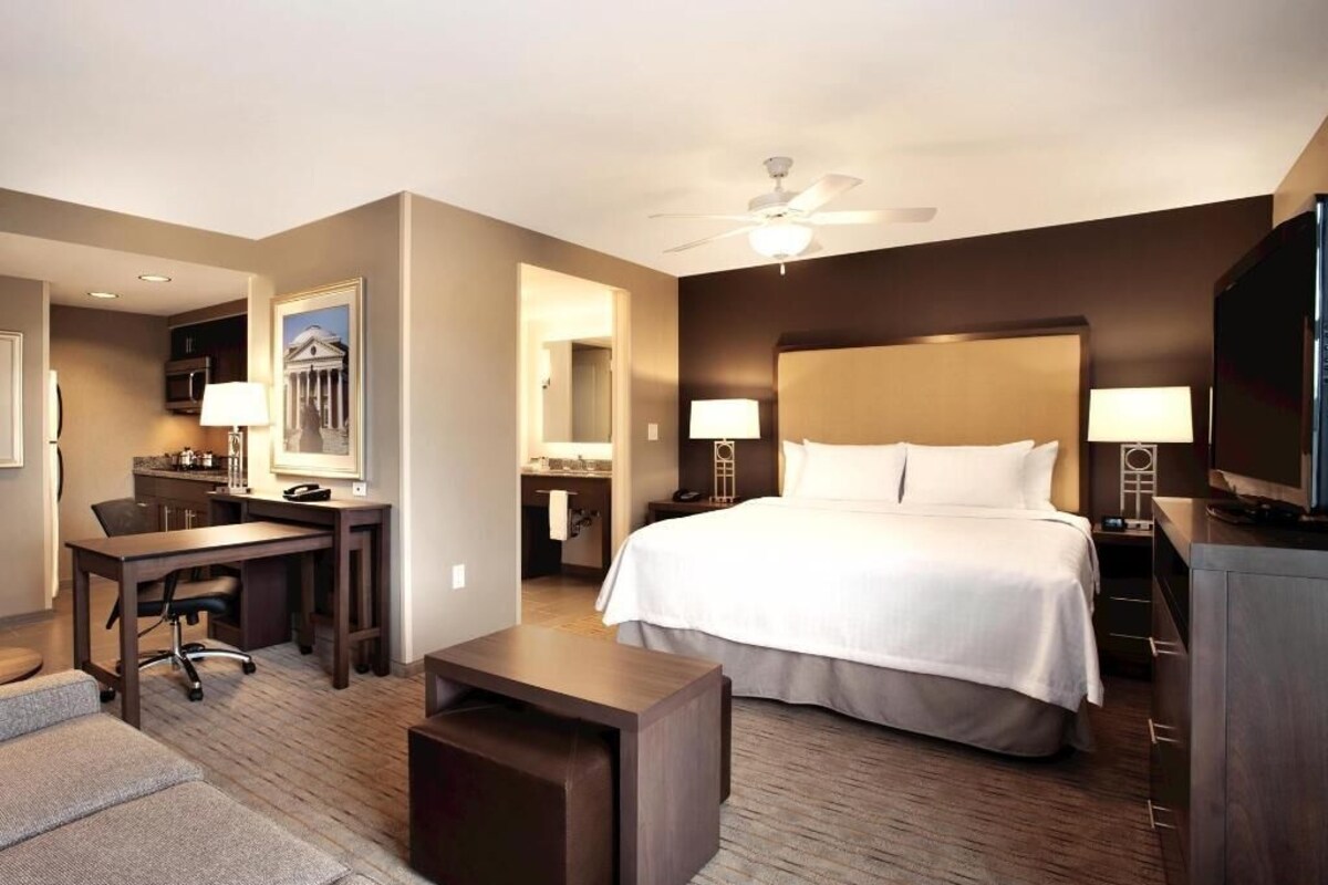 A hotel room with a bed, desk, chair, and a television.