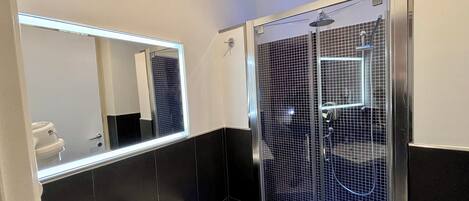 Un baño moderno con un lavamanos blanco, un espejo grande y una ducha con cerramiento de vidrio.