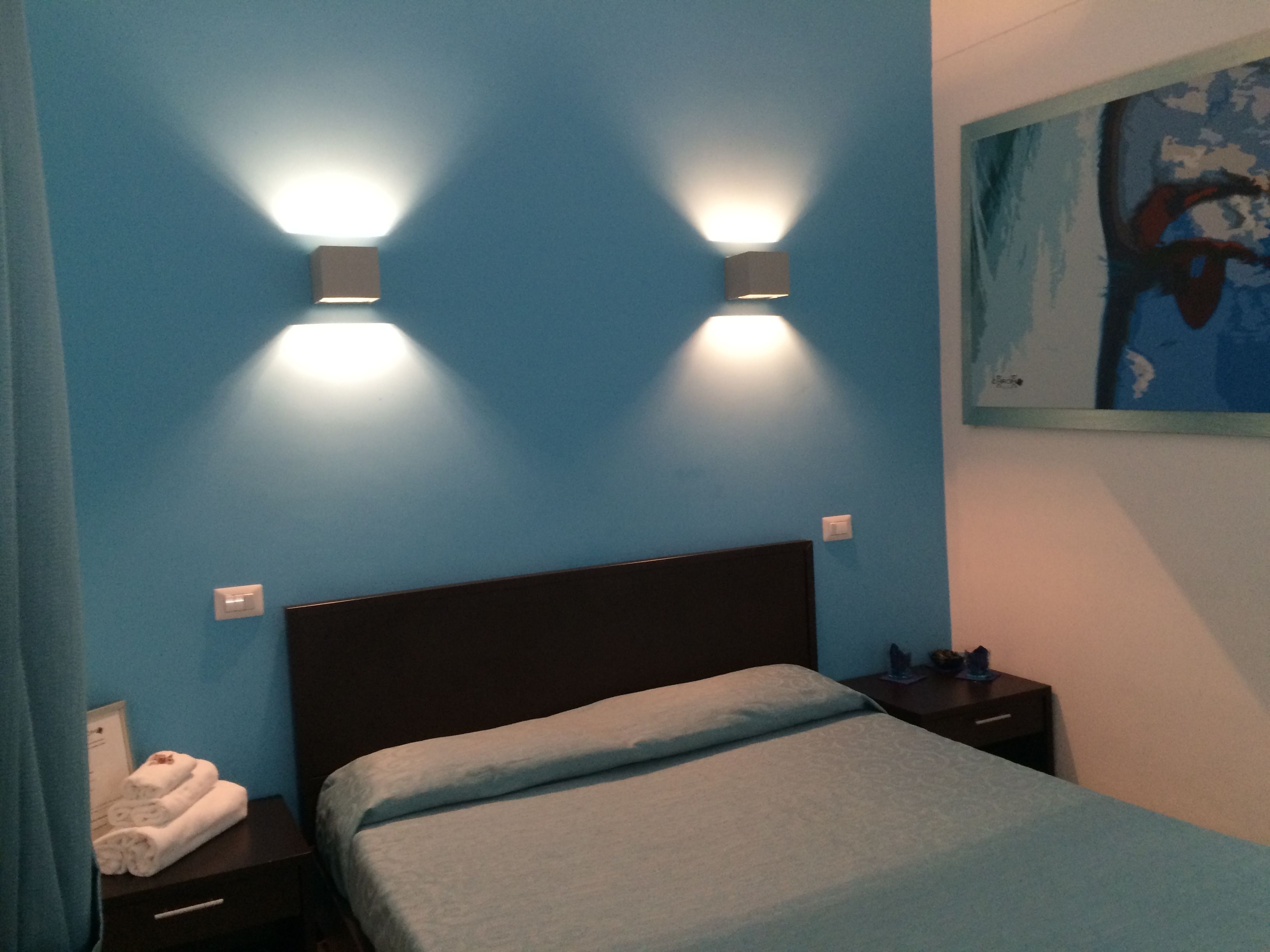 A bedroom with a bed, two bedside tables, a wall-mounted painting, and a blue wall.