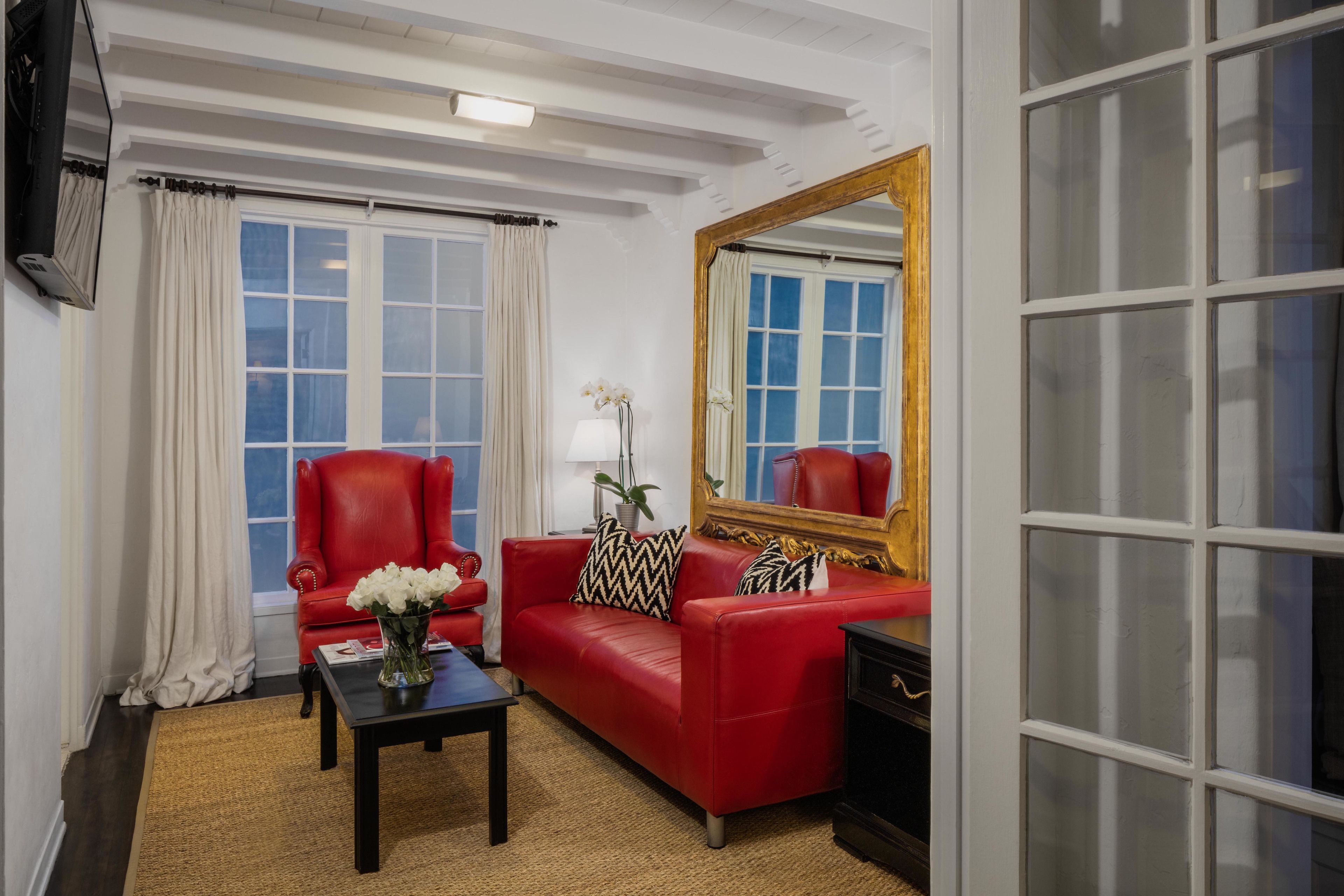 A room with a red sofa, a black coffee table, a mirror, and a window with white curtains.