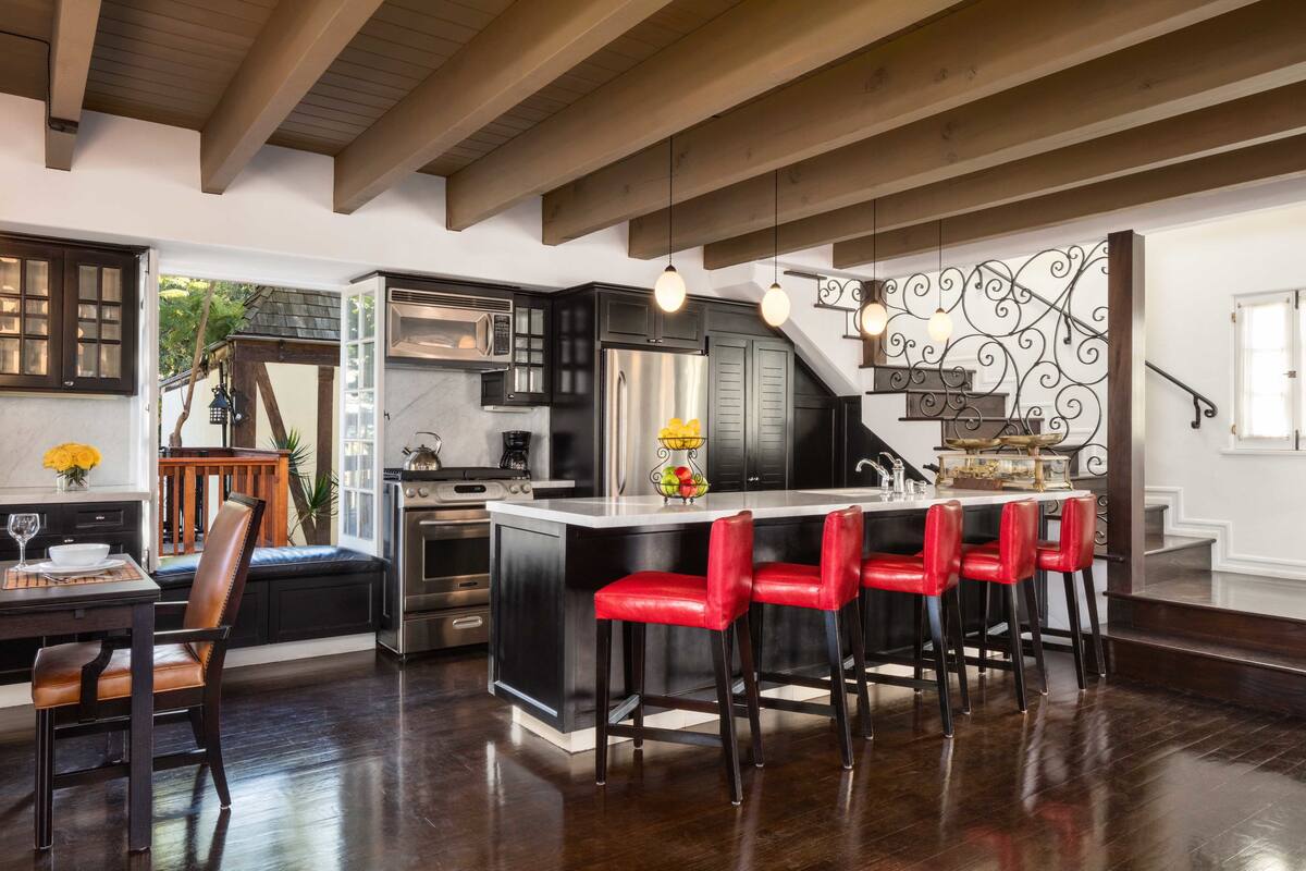 A modern kitchen with dark cabinetry, a central island with red bar stools, and a stainless steel refrigerator.