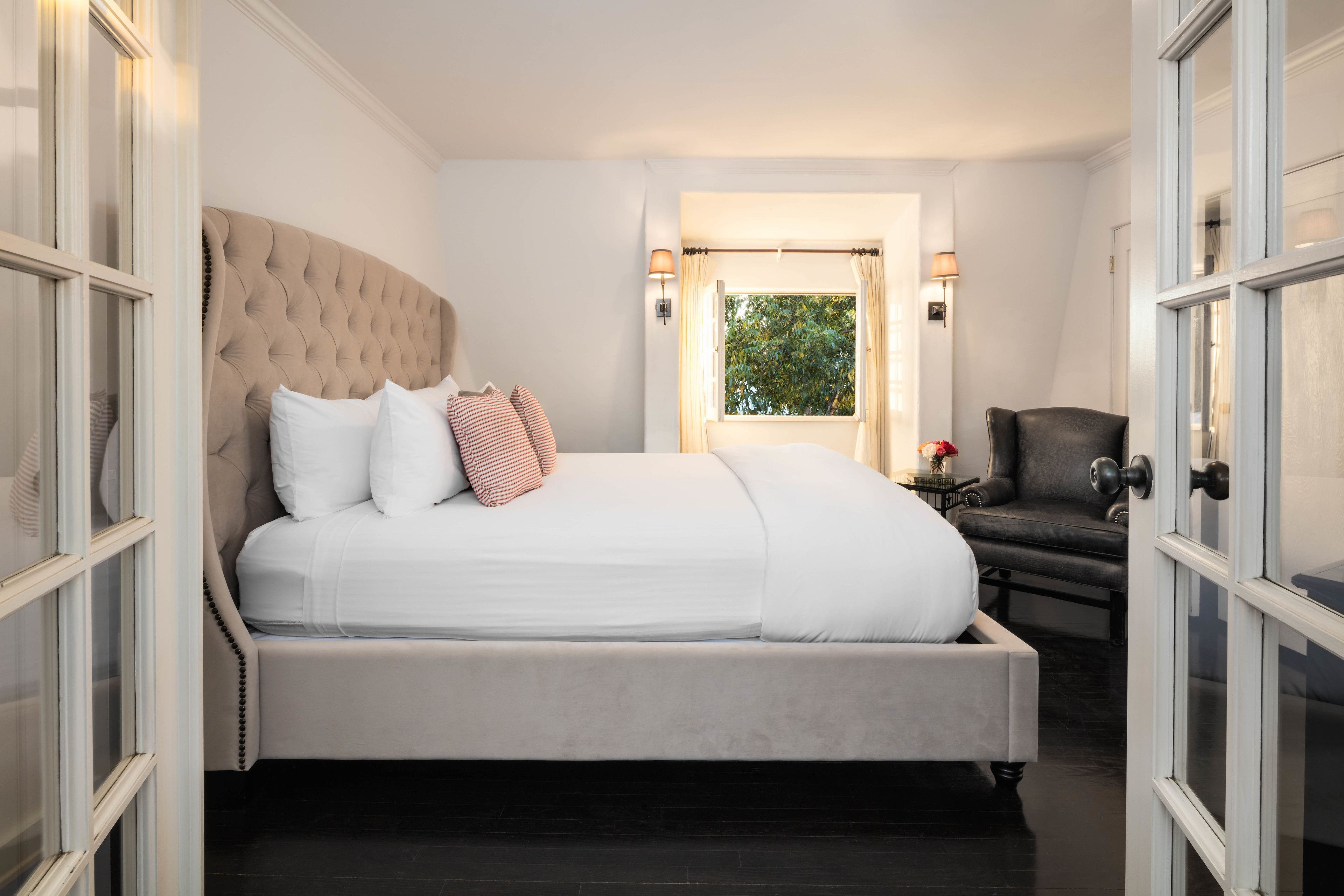 Quarto com cama grande, uma cadeira, mesa de cabeceira e janela com cortinas.
