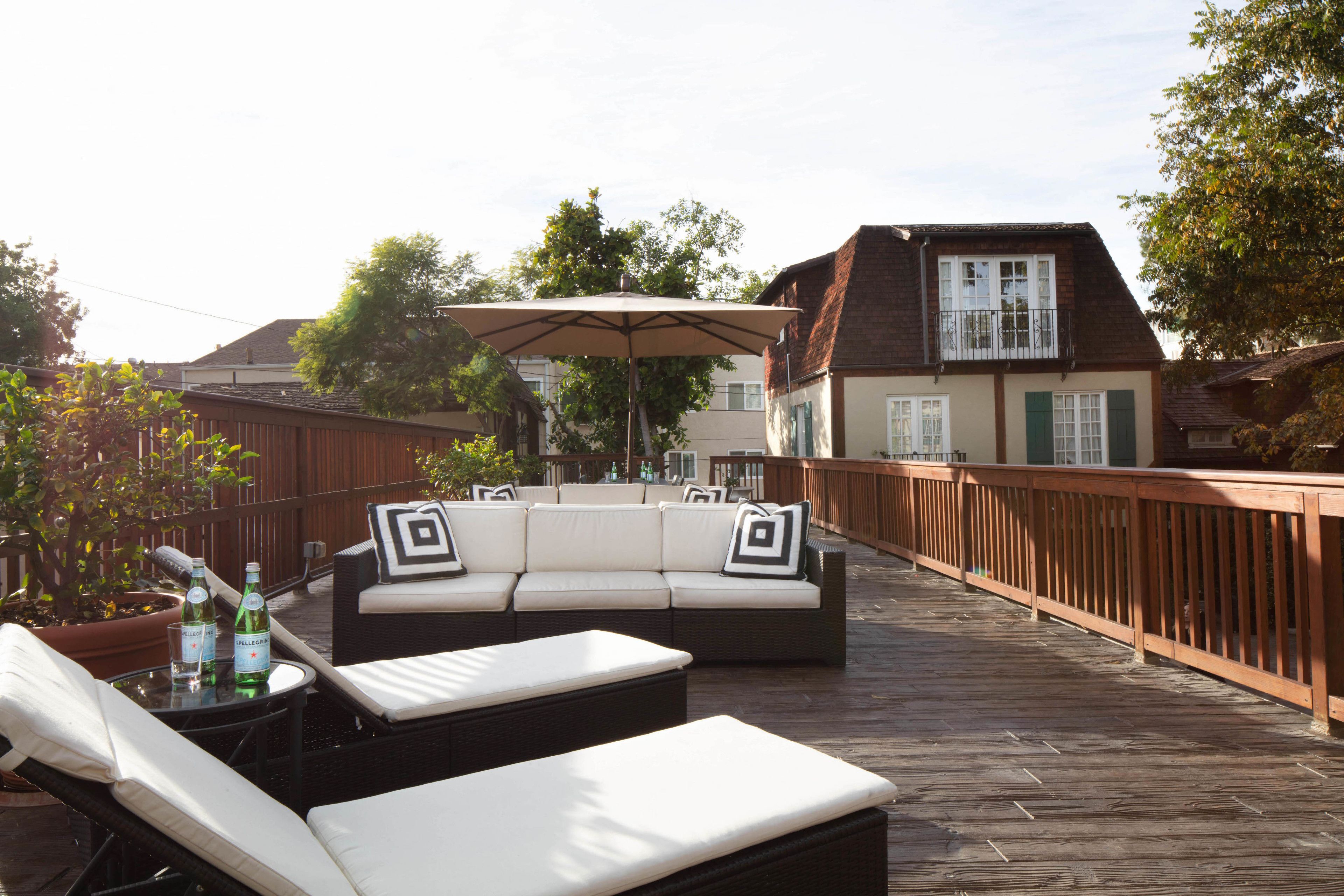 Une terrasse extérieure avec un canapé et des fauteuils de jardin, une rambarde en bois et un pot de fleurs.