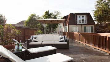 Une terrasse extérieure avec un canapé et des fauteuils de jardin, une rambarde en bois et un pot de fleurs.