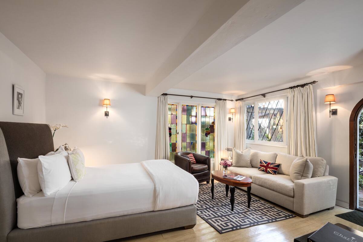 A hotel room with a bed, a sofa, a chair, a small table, and a window with curtains.