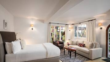 A hotel room with a bed, a sofa, a chair, a small table, and a window with curtains.