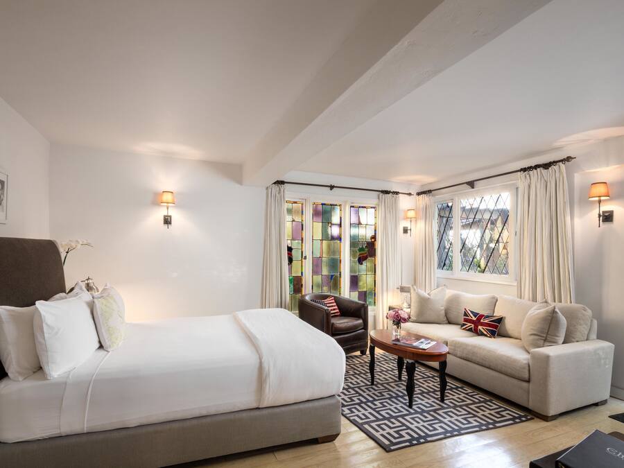 A hotel room with a bed, a sofa, a chair, a small table, and a window with curtains.