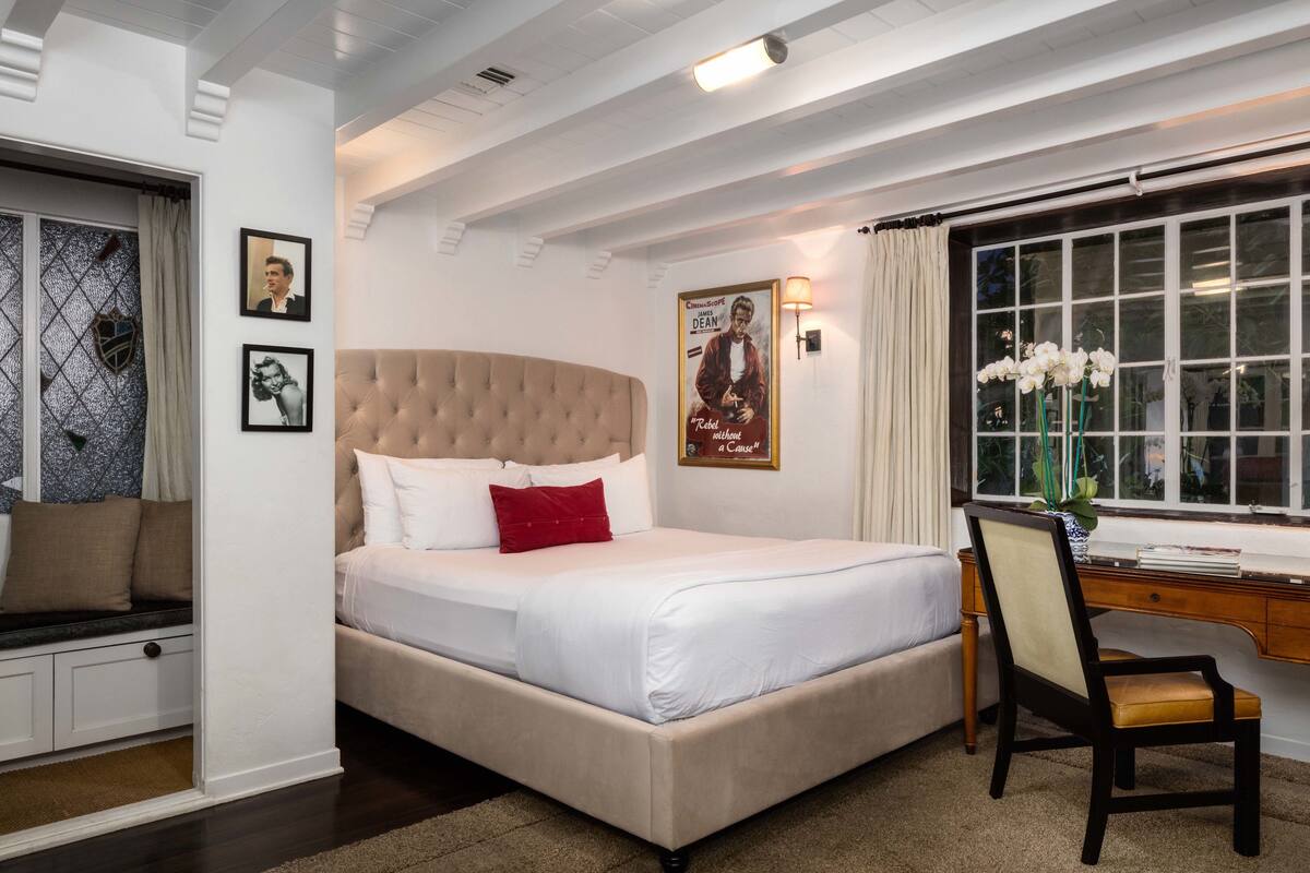 A neatly arranged bedroom with a large bed, a desk, and a window with curtains.