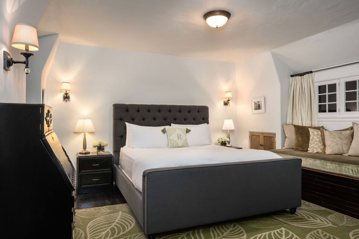 A bedroom with a large bed, bedside tables, a nightstand, a dresser, and a window with curtains.