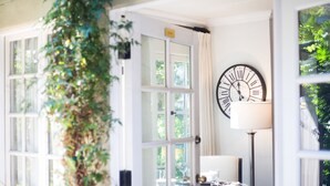 A room with a large window, a clock, and a table with a lamp. - The Charlie Hotel (West Hollywood)
