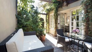 A patio with a wicker sofa, a glass table, and chairs. There is a potted plant and a door leading to an interior space. - The Charlie Hotel (West Hollywood)