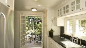 A kitchen with white cabinets, a black countertop, and a window with a view of greenery. - The Charlie Hotel (West Hollywood)