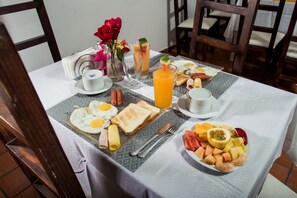 A breakfast table with eggs, toast, sausages, and a fruit plate. - Hotel Portes 9 (Santo Domingo)