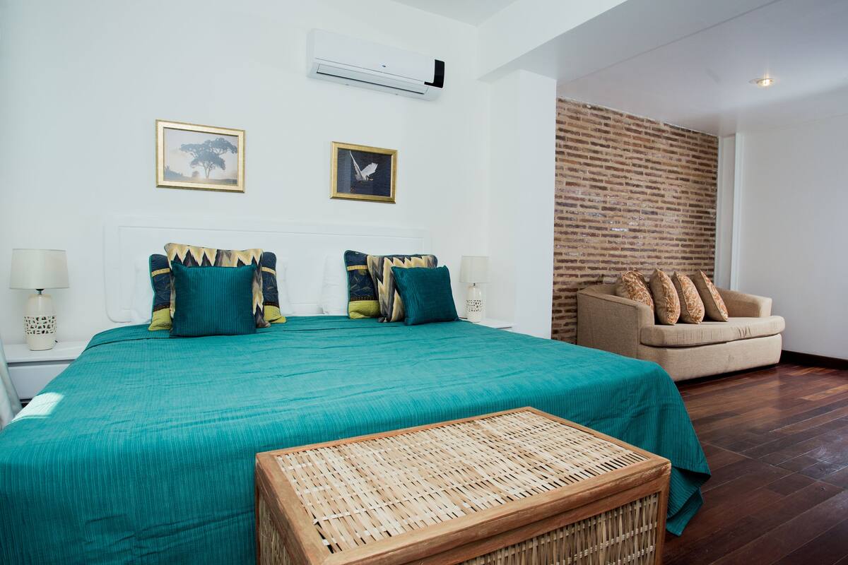 A bedroom with a large bed, two wall-mounted air conditioners, a sofa, and a wicker coffee table.