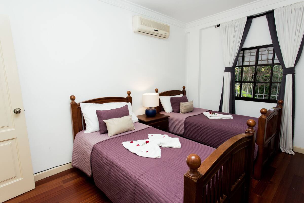 A hotel room with two beds, a window with curtains, and an air conditioning unit on the wall.