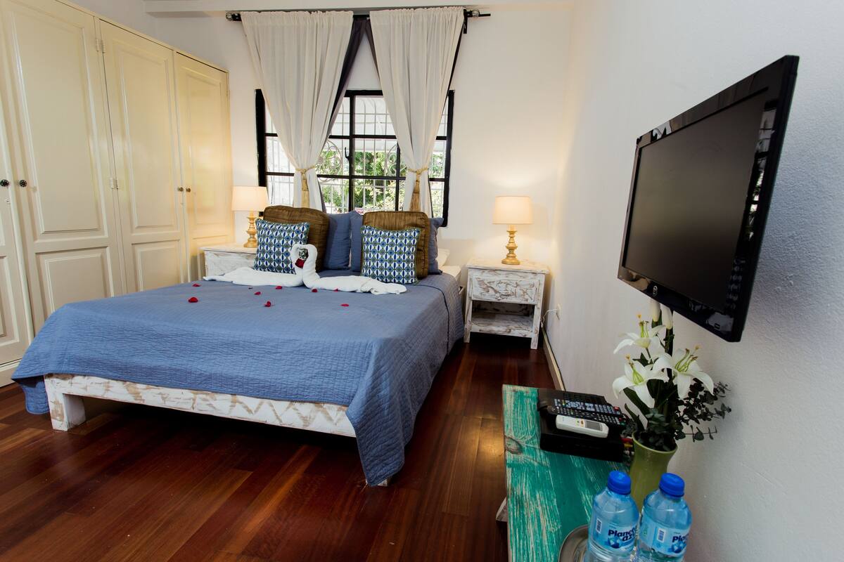 A bedroom with a bed, a TV, a nightstand, and a window with curtains.