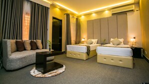 A hotel room with a sofa, two beds, a coffee table, and a bedside table with a lamp. - Hotel Tropical Daisy (Dhaka)