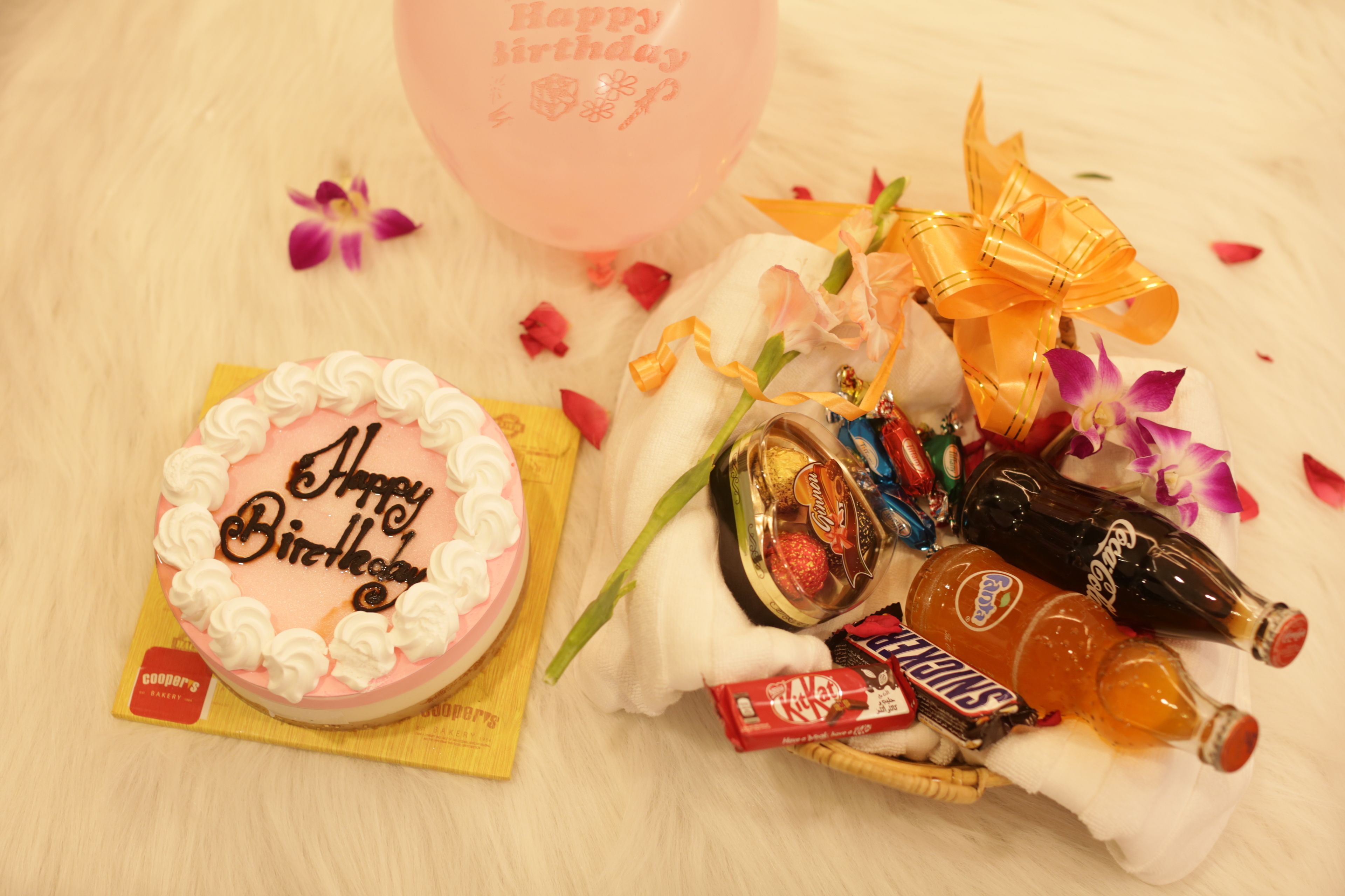 Un pastel de cumpleaños con la frase 'Happy Birthday' escrito, rodeado de diversos bocadillos y bebidas.