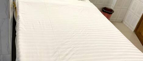 A neatly made bed with white bedding in a room with white tiled walls and a black headboard.