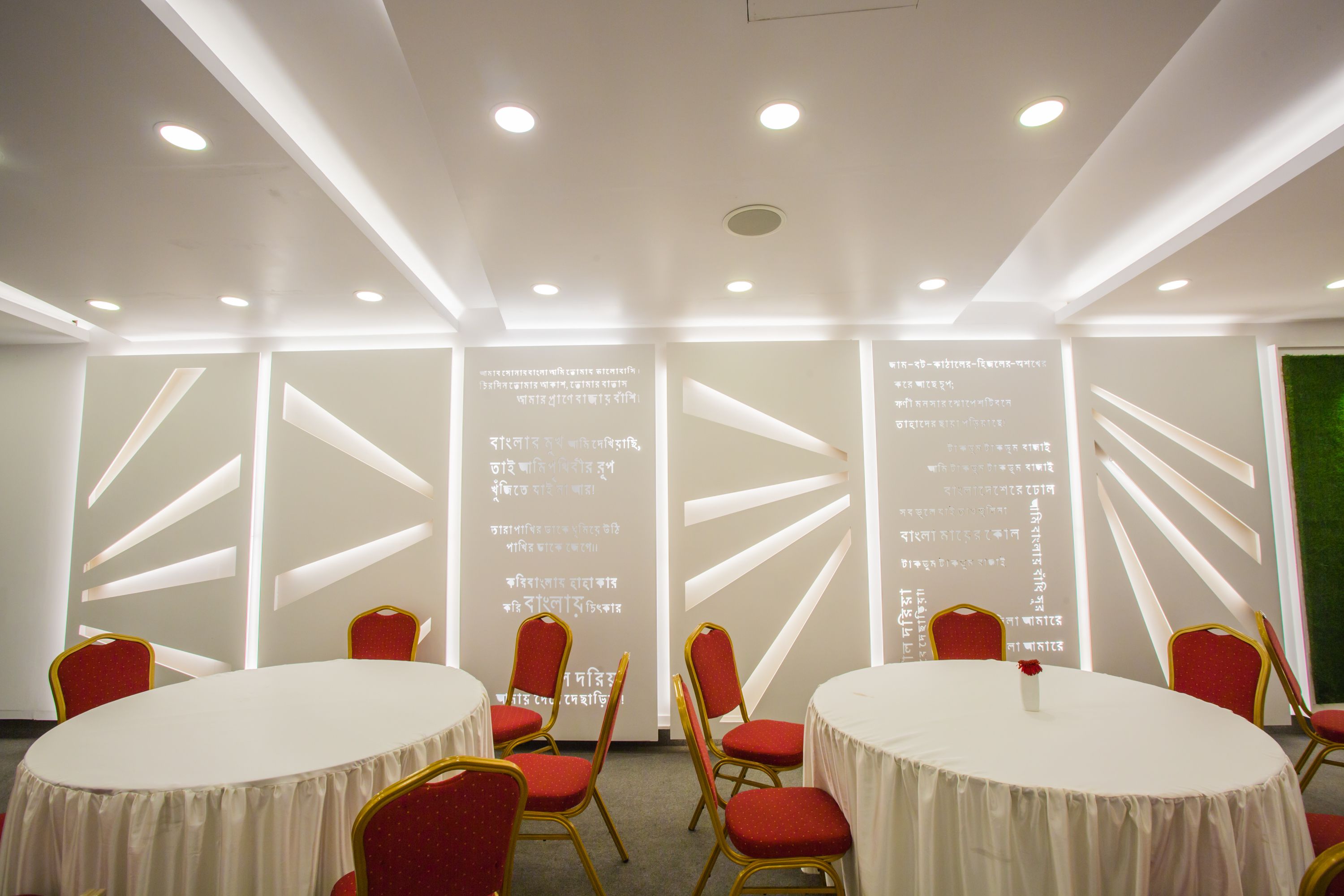 Un salón de conferencias con mesas blancas y sillas rojas, que destaca por un diseño de techo moderno e iluminación empotrada.