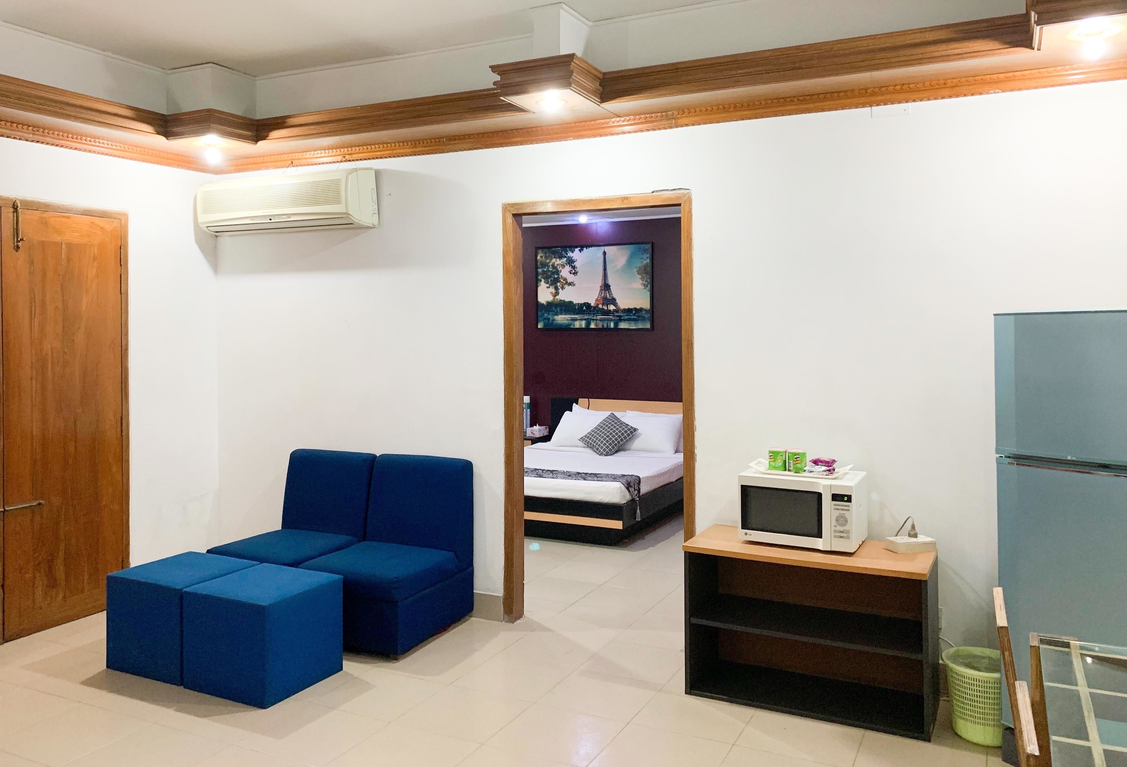 Una habitación con una cama, un sofá azul, un microondas y un televisor en la pared.