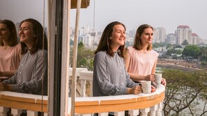 A balcony with a city view, a white railing, and a person holding a mug. - Hotel Tropical Daisy (Dhaka)