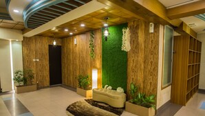 A lobby with a wooden wall, a green wall, a sofa, and potted plants. - Hotel Tropical Daisy (Dhaka)