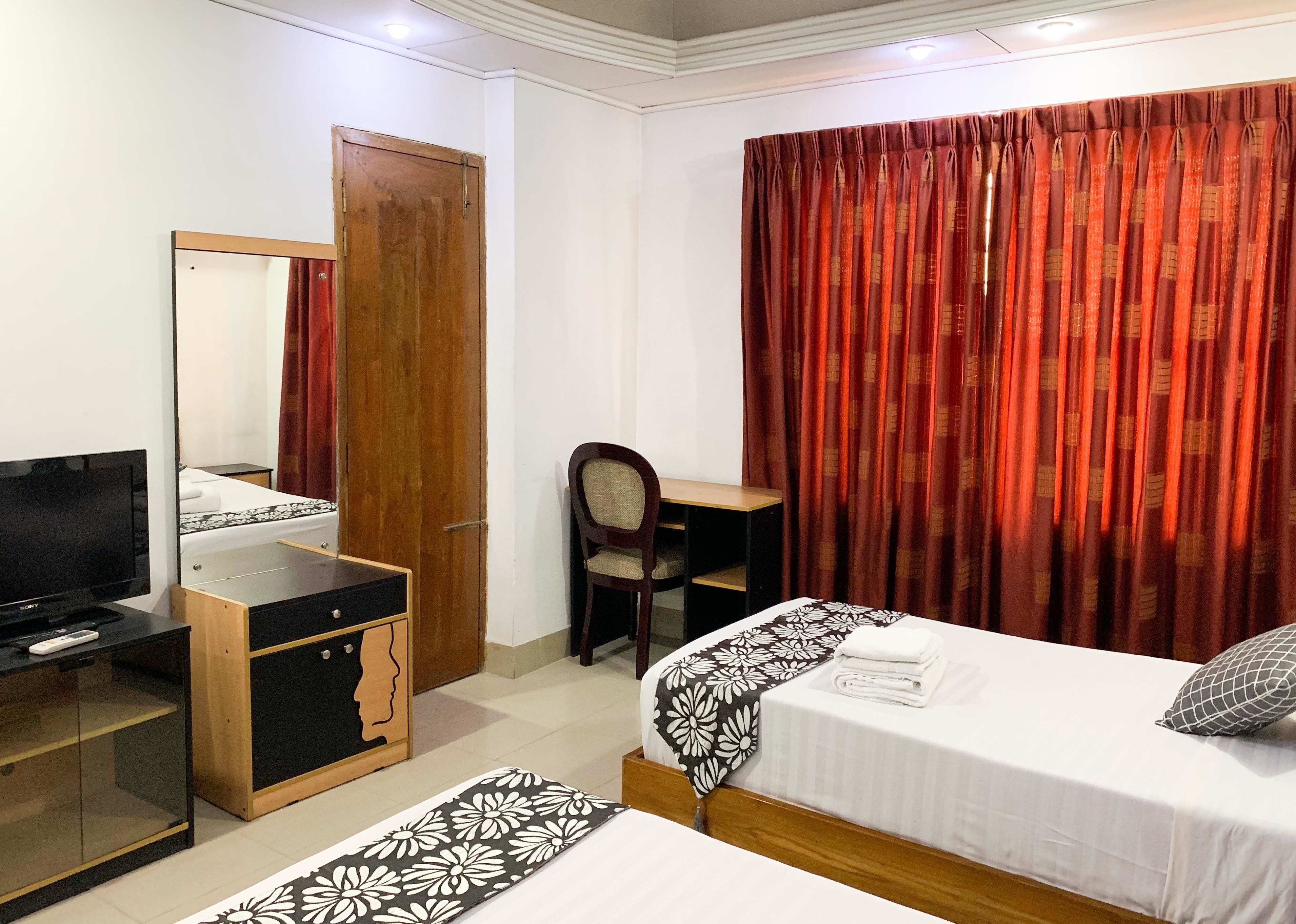A hotel room with a bed, a desk, a chair, a TV, and a wardrobe.