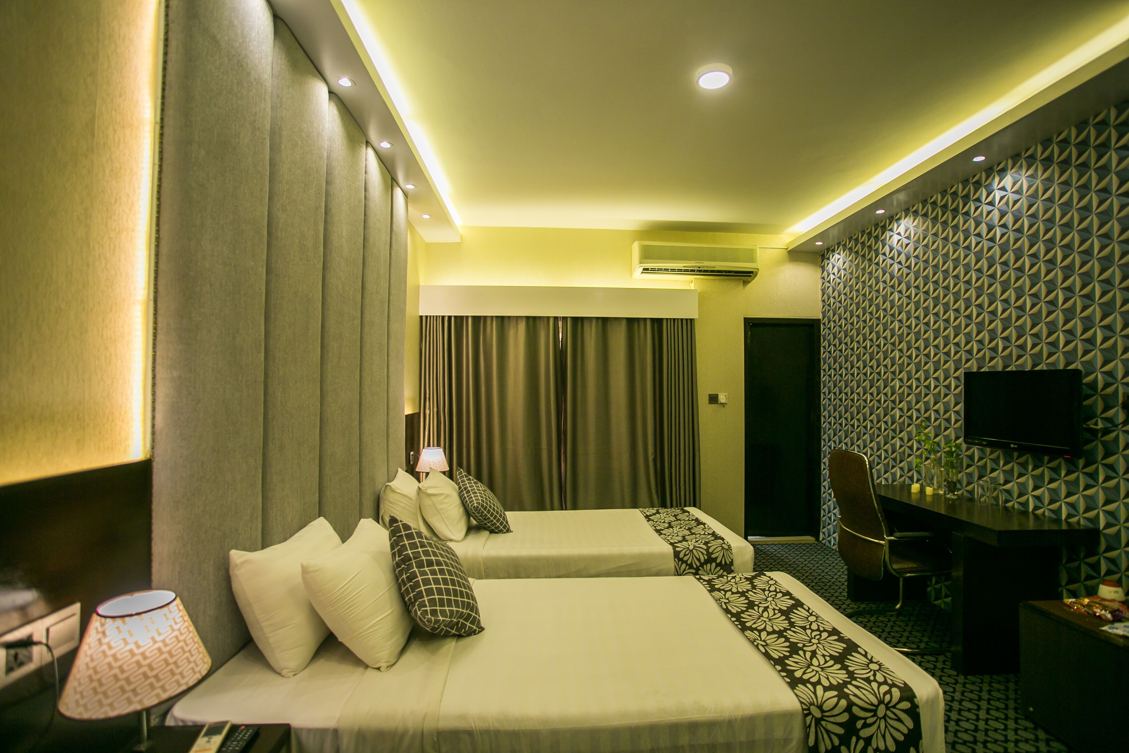 A hotel room with two beds, a desk, a TV, and a lamp.