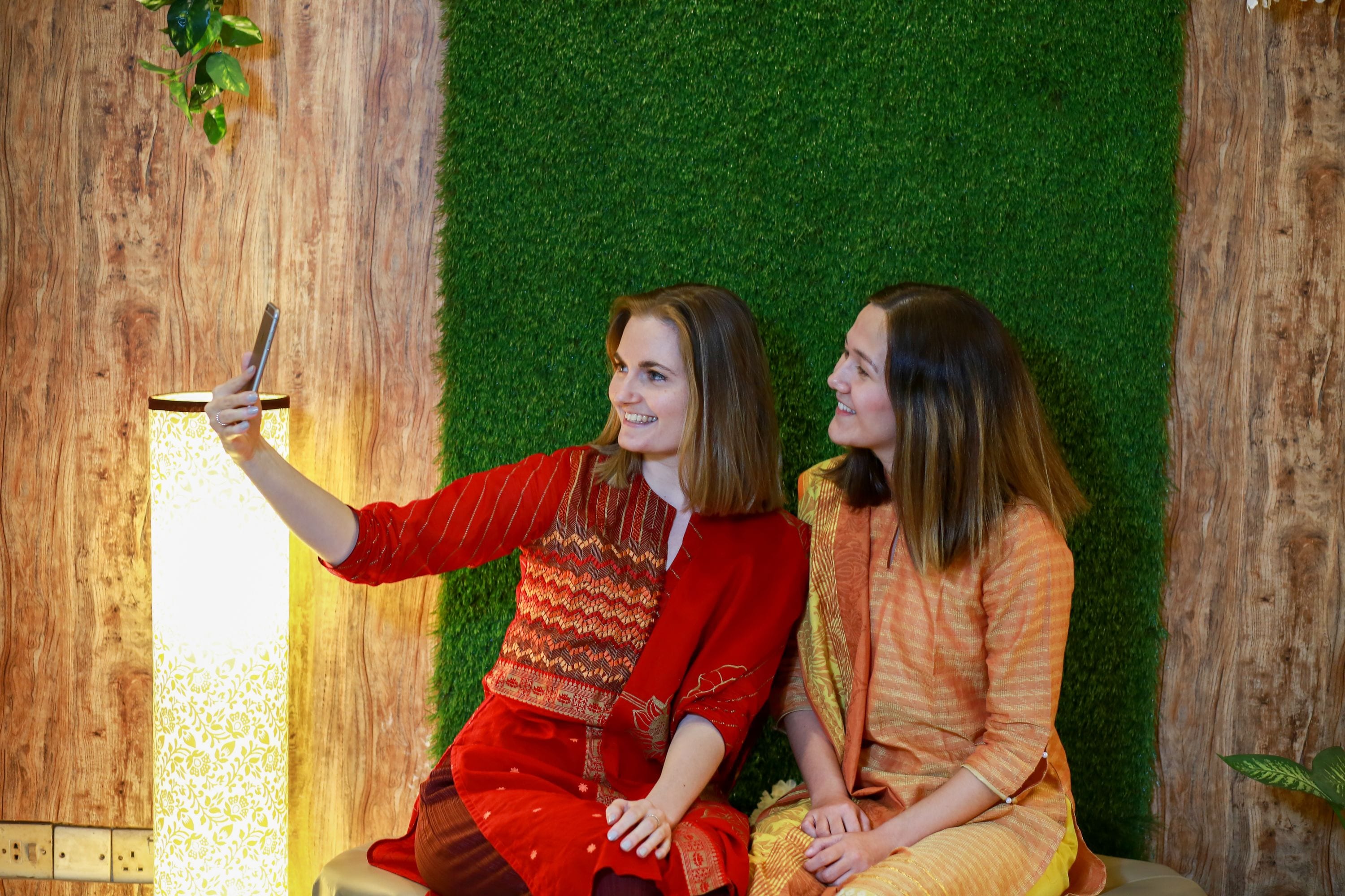 Two individuals seated against a backdrop of a wooden wall and a green wall.