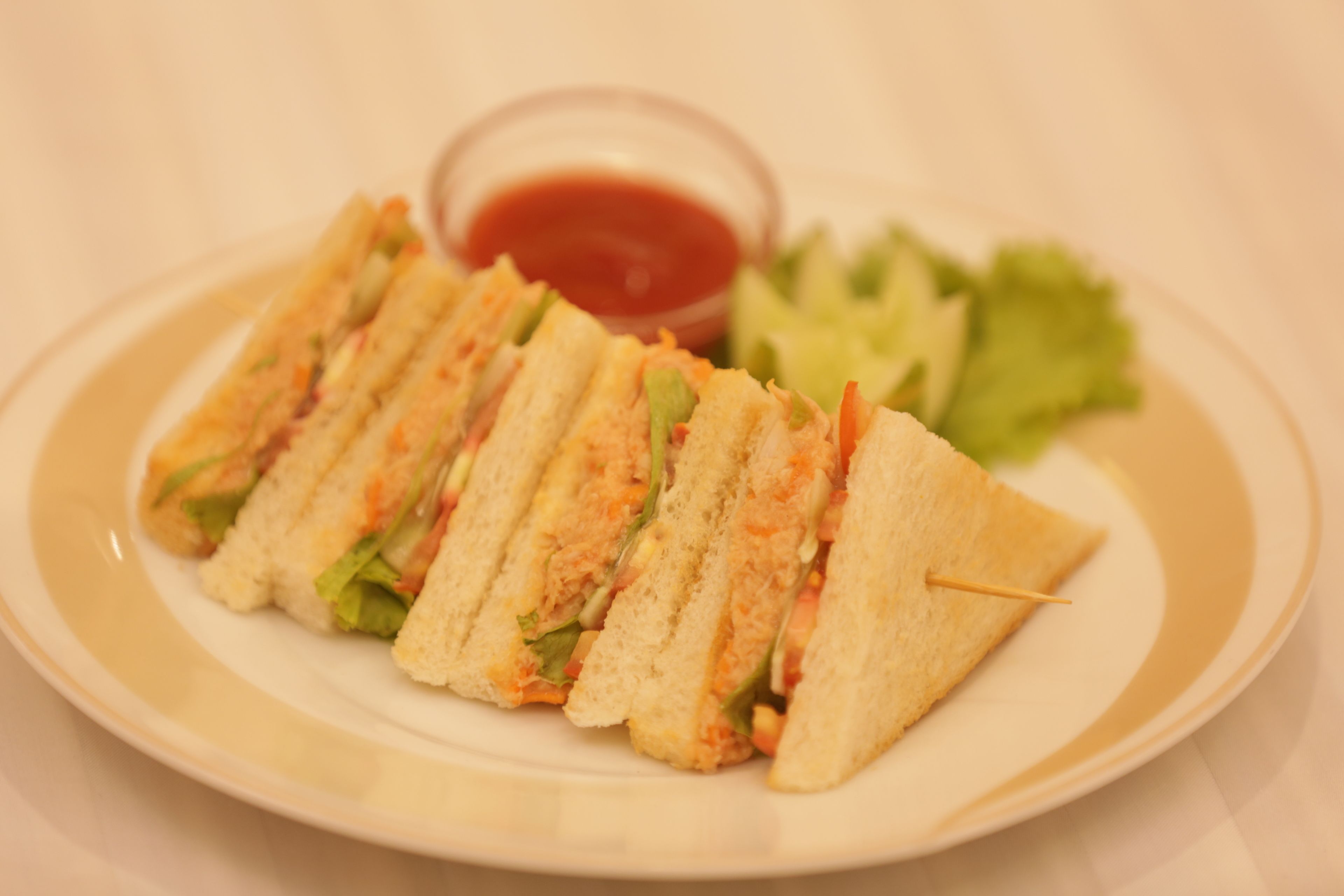 A plate with a sandwich cut into triangles, a small bowl of sauce, and a side of lettuce.