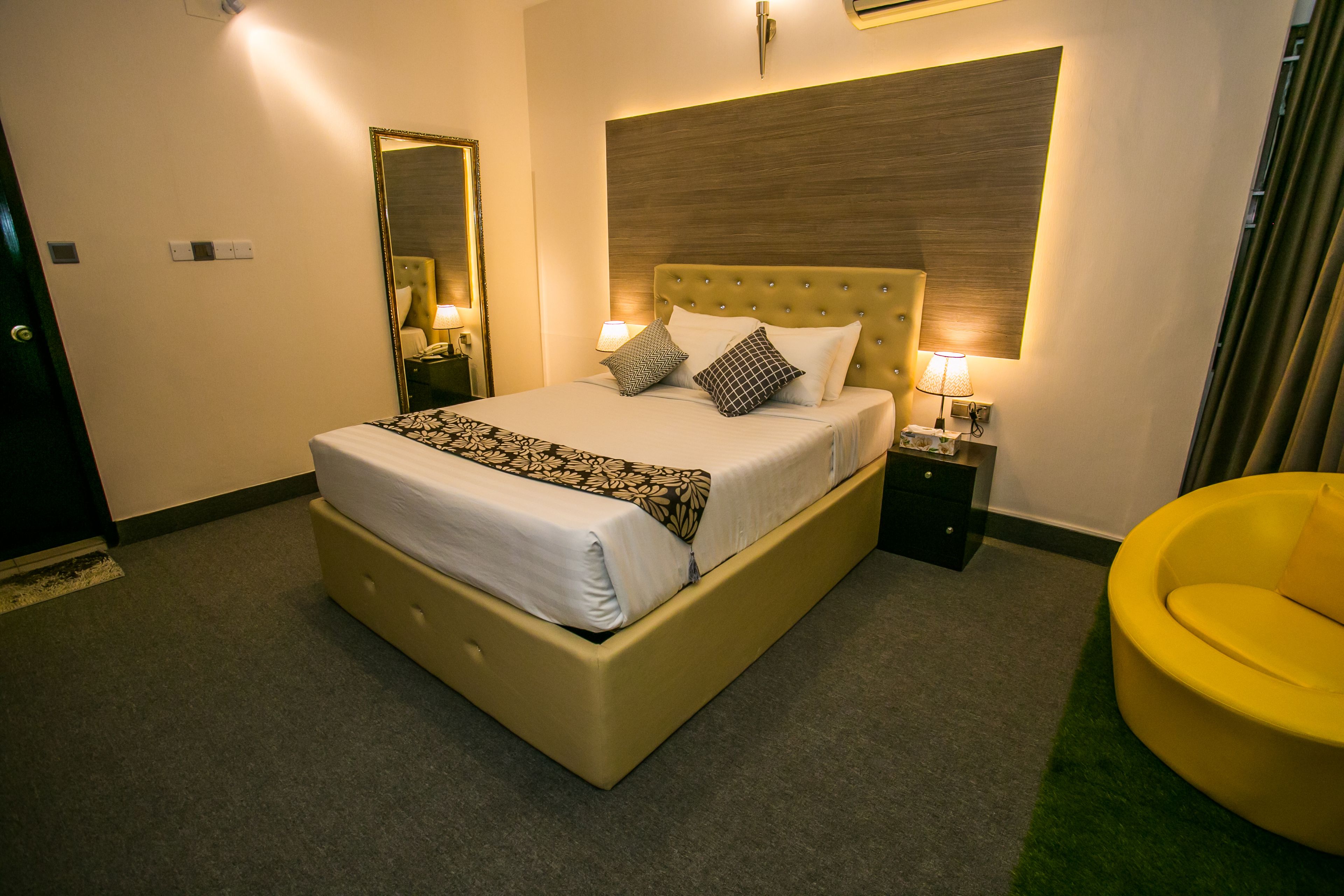Ein Hotelzimmer mit einem großen Bett, Nachttischlampen, einem Spiegel und einem gelben Sessel.