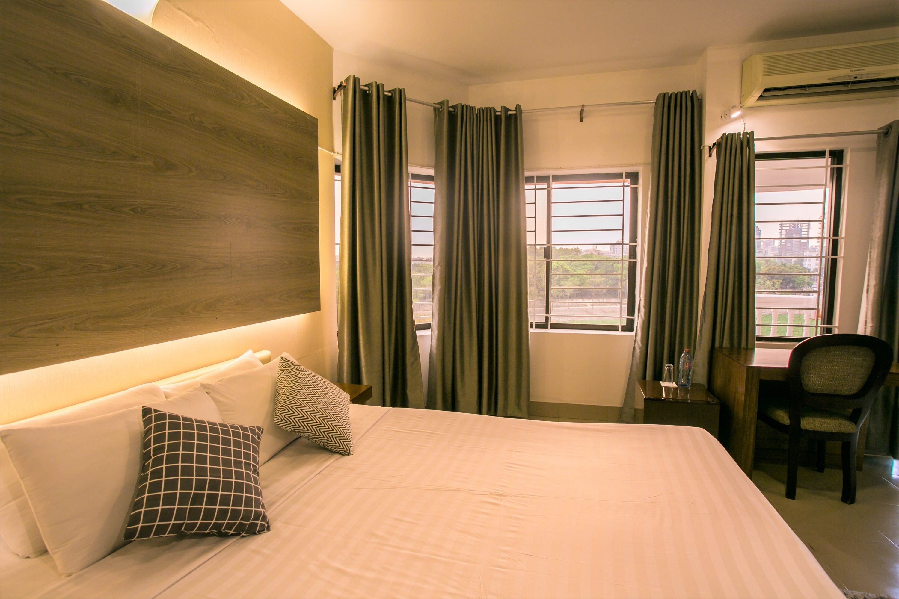 A hotel room with a large bed, two pillows, a desk, a chair, and a window with curtains.