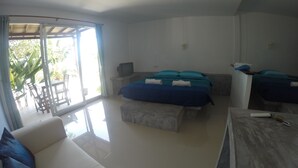 A modern hotel room with a sofa, a bed with blue bedding, a TV, and a balcony with a table and chairs. - Moon Beach Resort (Ko Pha-ngan)