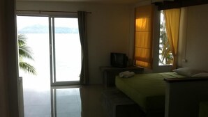 A hotel room with a bed, a television on a nightstand, and a view of the sea through a large window. - Moon Beach Resort (Ko Pha-ngan)