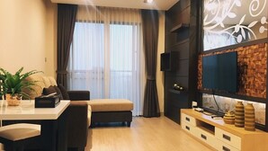 A modern living room with a sofa, a dining table, and a TV on a wooden stand. - De Richy Chiang Mai (Hang Dong)