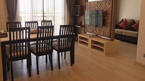 A dining area with a table and chairs, a television mounted on a brick wall, and a sofa in the background. - De Richy Chiang Mai (Hang Dong)