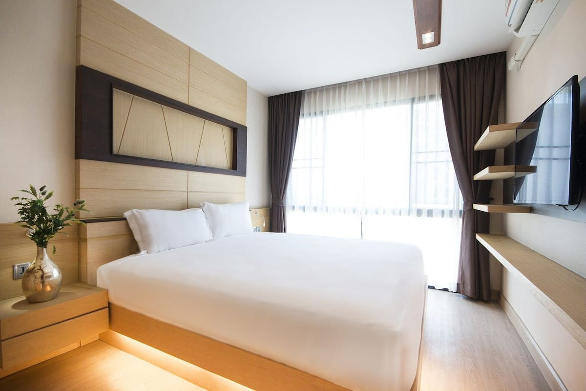 A modern hotel room with a large bed, a flat-screen TV mounted on the wall, and a bedside table with a vase of flowers.