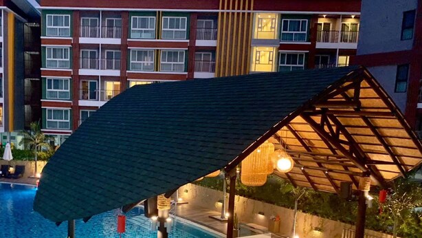 A poolside bar with a thatched roof, surrounded by a pool and a building with multiple balconies. - De Richy Chiang Mai (Hang Dong)