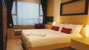 A hotel room with a large bed, a bedside table, a nightstand, a window with sheer curtains, and a headboard. - De Richy Chiang Mai (Hang Dong)