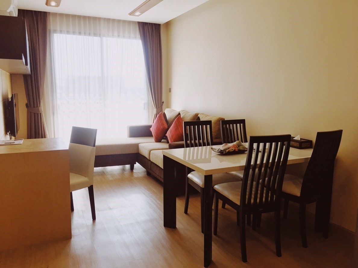 A modern living room with a sofa, dining table, and chairs. There is a TV on a stand and a window with curtains.