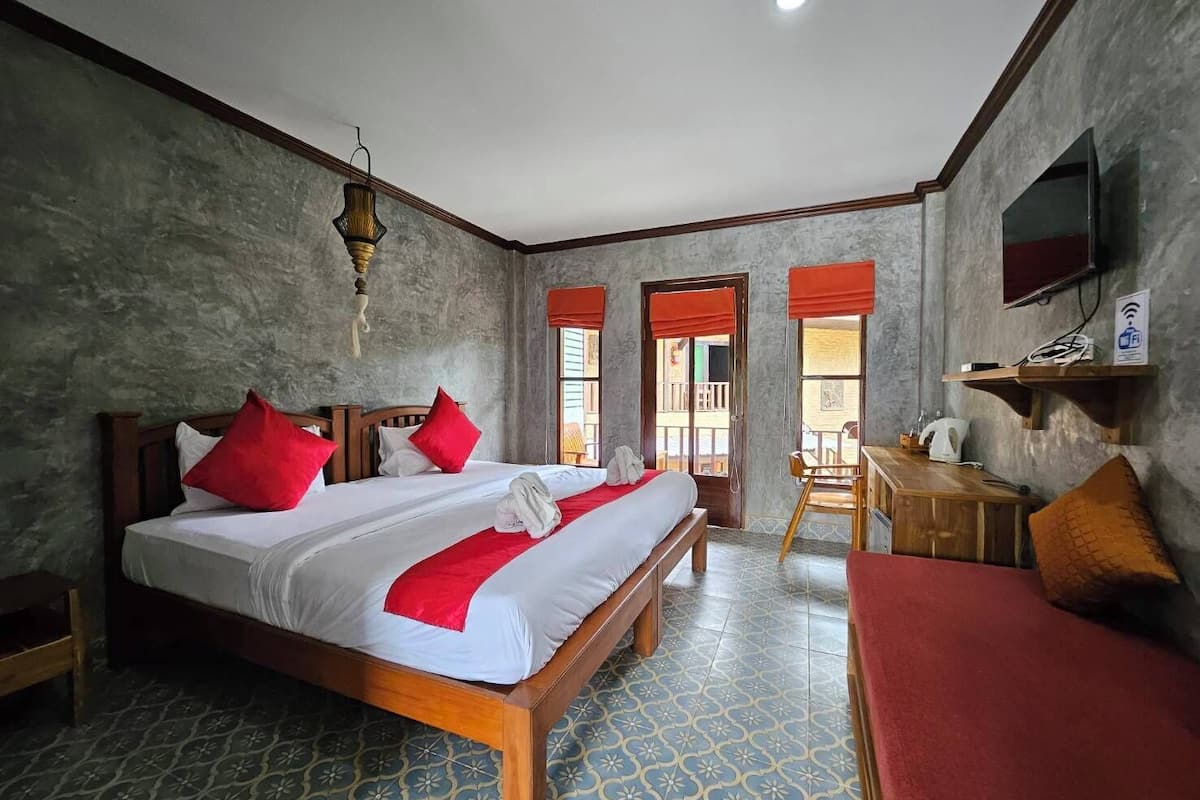 Une chambre d’hôtel avec un grand lit, un bureau en bois, une télévision et un balcon agrémenté de rideaux rouges.