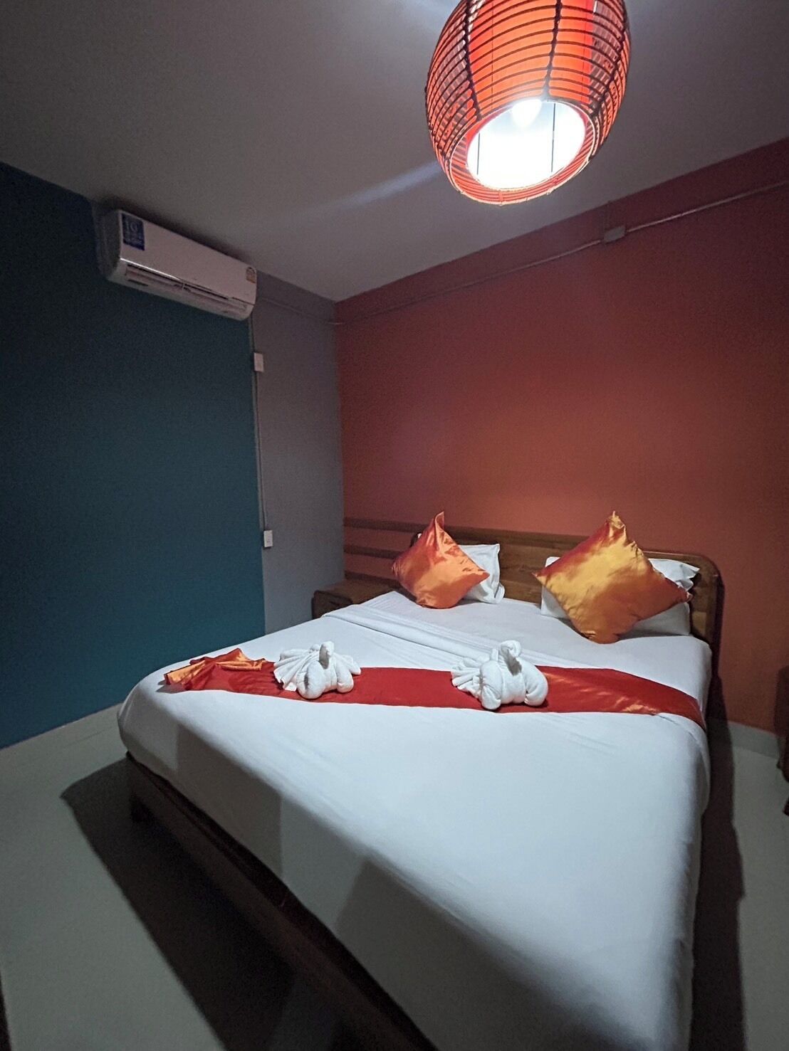 Quarto de hotel com cama, almofadas, colcha vermelha e branca, e luminária pendente vermelha.