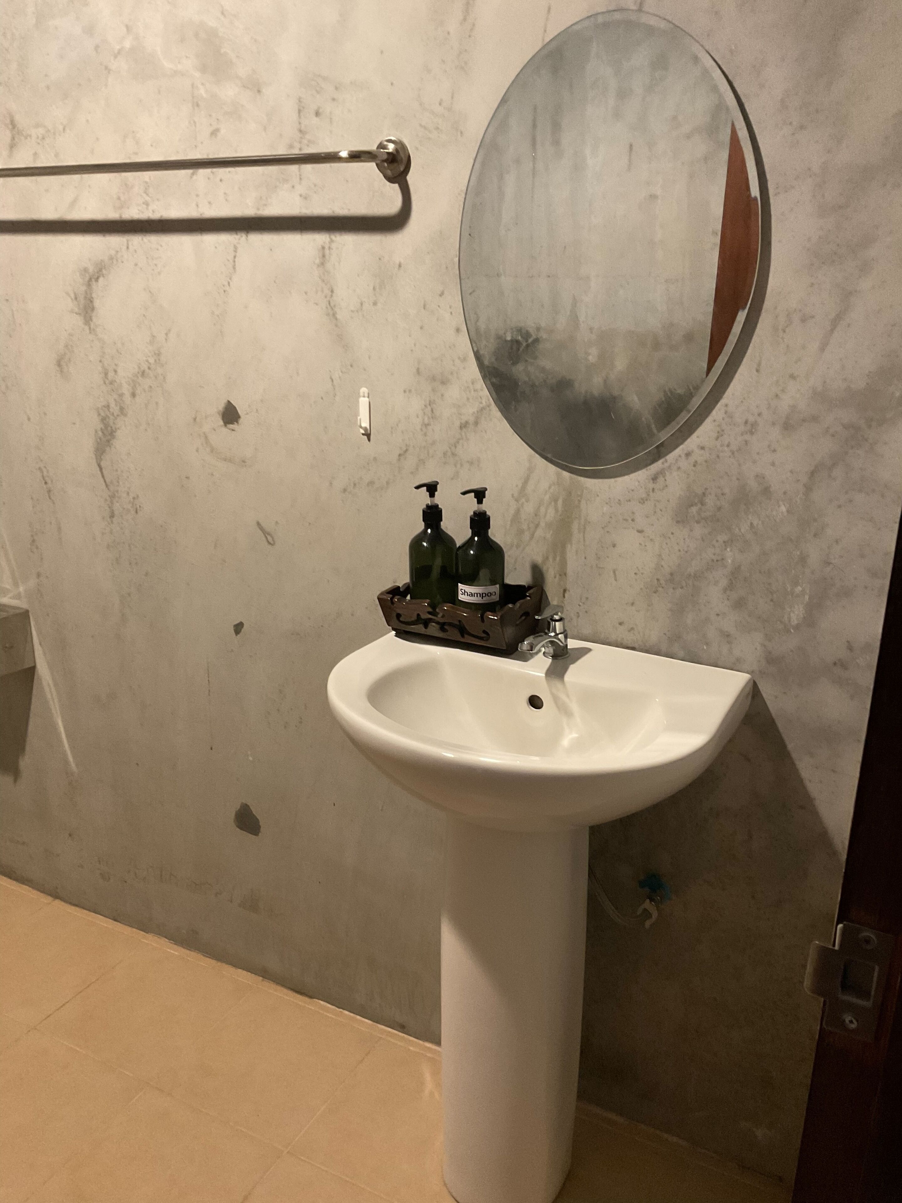 A bathroom with a white sink, two shampoo bottles, a round mirror, and a towel rack.
