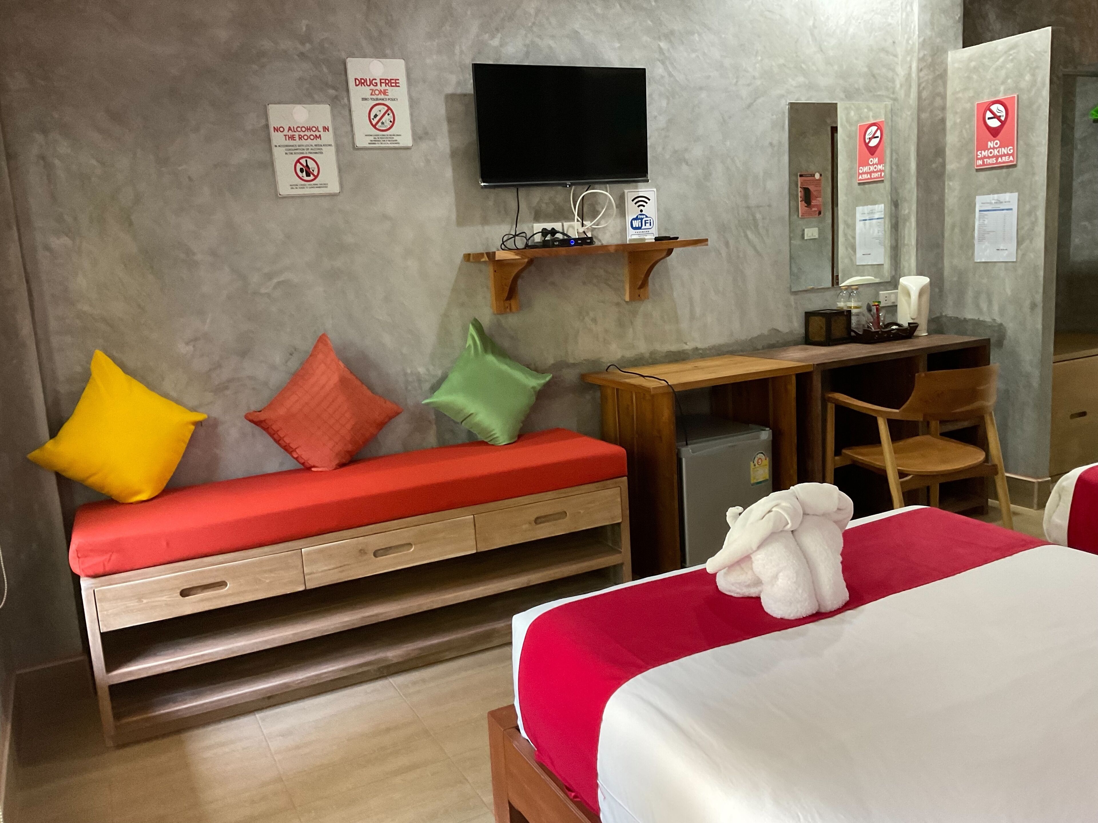 Habitación de hotel con cama, escritorio, televisor y sofá con cojines de colores.