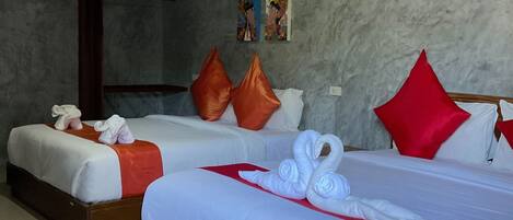 A hotel room with two beds, each with white linens and red accents, a grey textured wall, and a wooden floor.