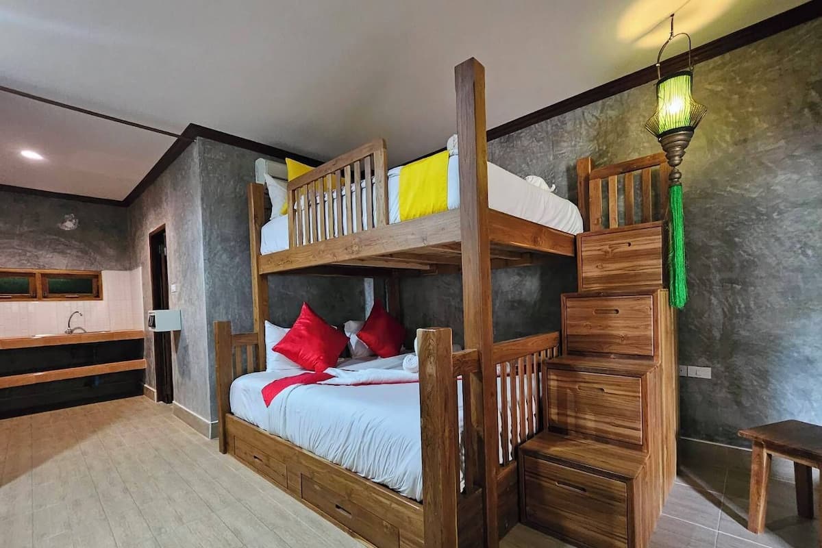 Un lit superposé avec une structure en bois, un petit bureau et une lampe verte suspendue.