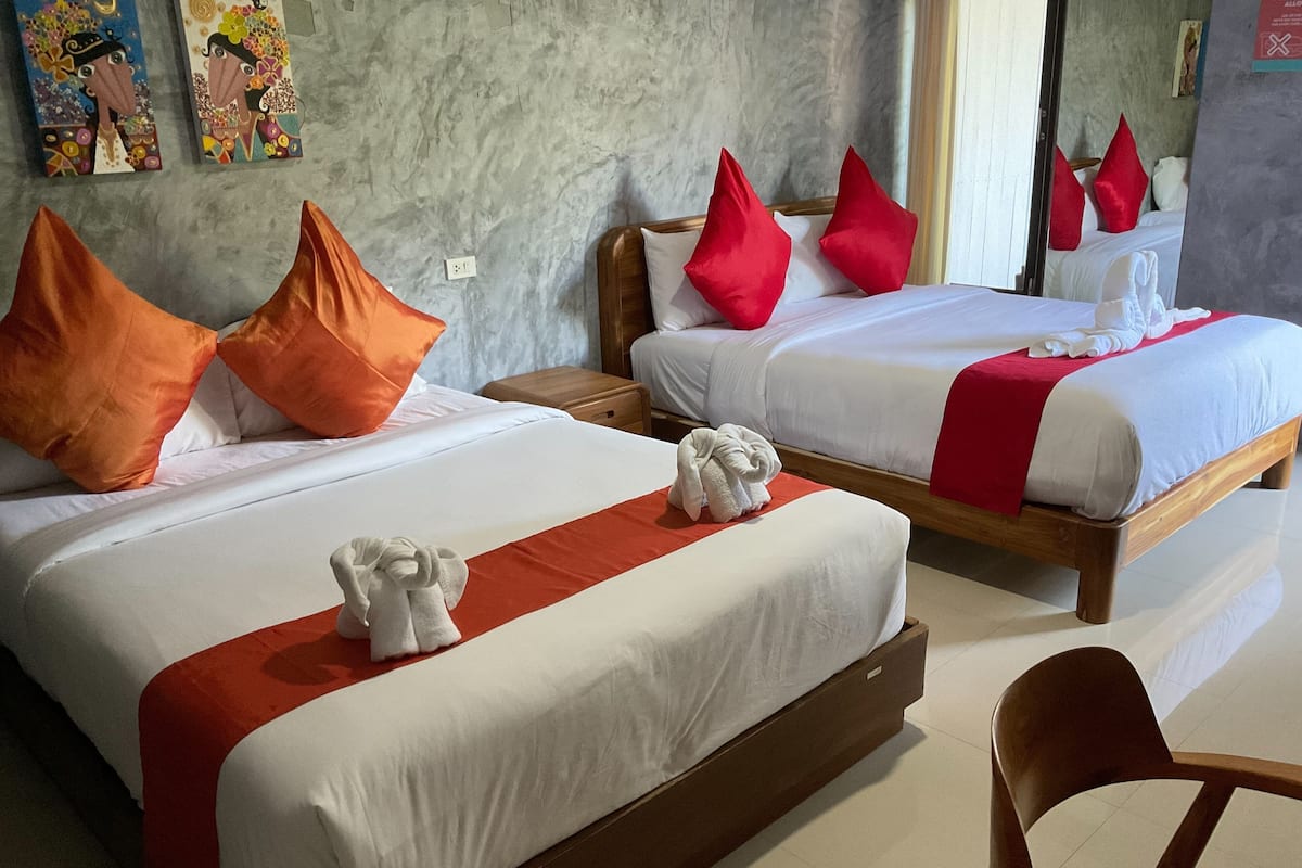 Une chambre d’hôtel avec deux lits, chacun étant équipé de draps blancs et d’oreillers rouges. On trouve des serviettes sur les lits et une chaise en bois dans la pièce.