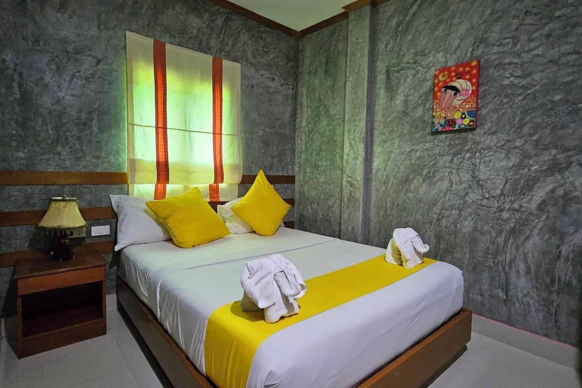 Une chambre d’hôtel avec un grand lit, deux oreillers, une table de chevet, une lampe et une œuvre d’art colorée accrochée au mur.