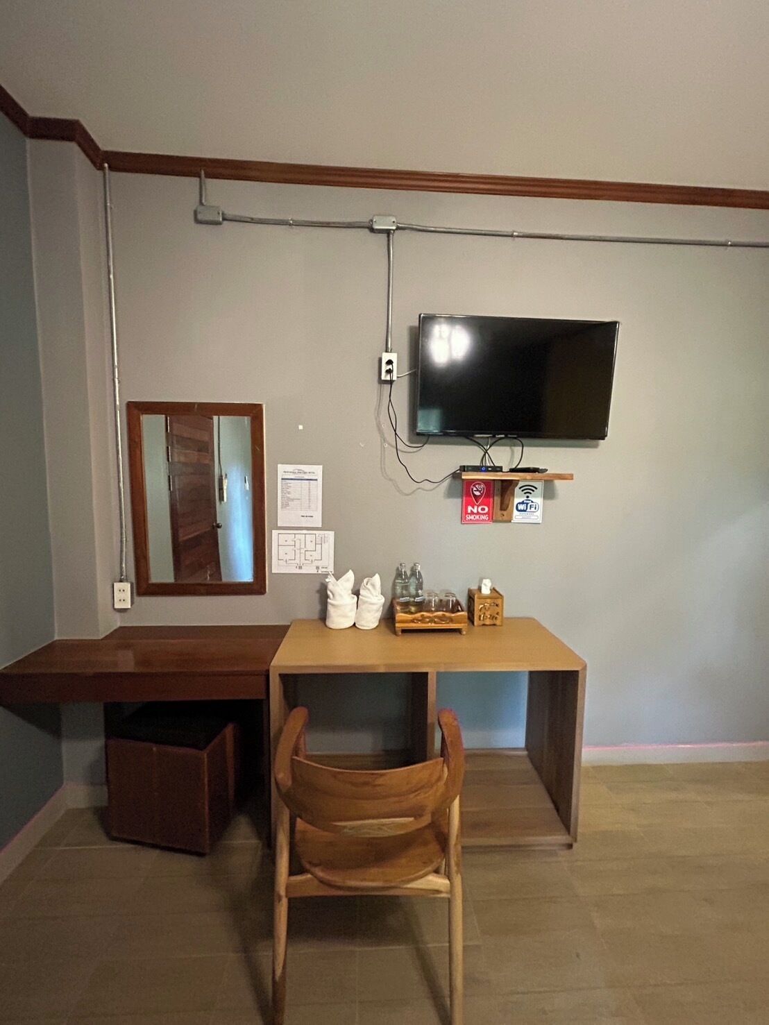Une pièce comprenant un bureau en bois, un téléviseur fixé au mur, un miroir et un banc.